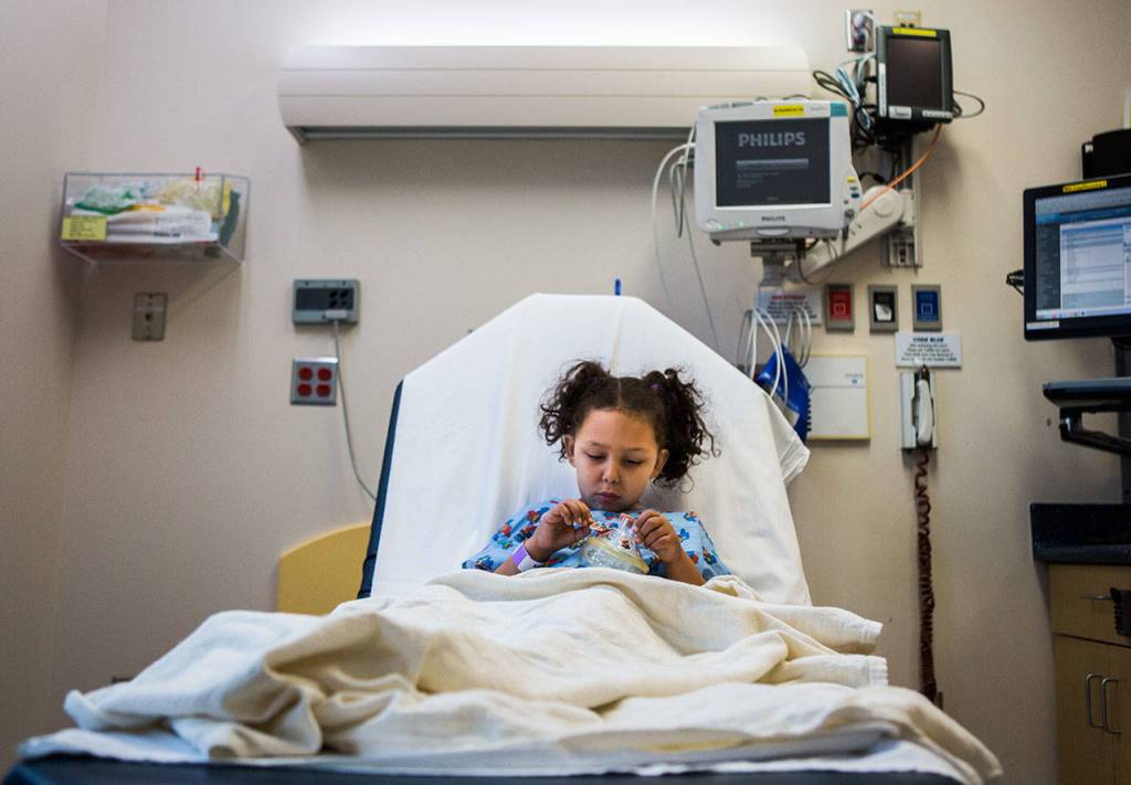 Kaya sits in a hospital bed at Seattle Childrens Hospital and places car stickers on her anesthesia mask while she waits to be taken in for her MRI on Dec. 12, 2018. This is Kayas first brain scan since she stopped radiation to treat her brain tumor. (Olivia Vanni / The Herald)