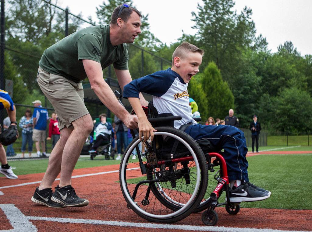 Ryan Lawrence Barton, 11, yells after getting a hit, while his buddy helps push him to first base. (Olivia Vanni / The Herald)