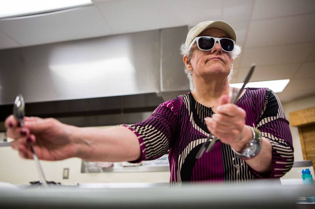 <a href="https://www.heraldnet.com/news/blind-and-deaf-and-independent-thanks-to-a-local-agency/" target="_blank">Debbie Curry</a> feels how many and what kind of utensils she has as she wraps napkins during her volunteer session at the Carl Gipson Senior Center on May 16 in Everett. (Olivia Vanni / The Herald)