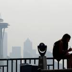 In this 2018 photo, a girl works on a drawing next to an unused viewing scope as a smoky haze obscures the Space Needle and downtown Seattle behind. Tens of millions of people in the Western US face a growing health risk due to wildfires as more intense and frequent blazes churn out greater volumes of lung-damaging smoke, according to research scientists at NASA and several major universities. (AP Photo/Elaine Thompson, File)