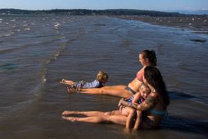 Milissa Simons, right, holds Jet Juliann while Ashley Elledge, center, watches Lincoln Ballard swim in the water off of Jetty Island last year. (Herald file)
