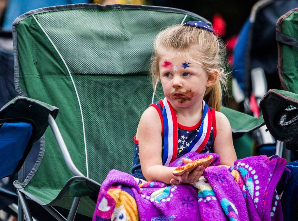 A young girl with pizza sauce and donut glaze on her face watches the parade during the Colors of Freedom Fourth of July Parade on Thursday, July 4, 2019 in Everett, Wash. (Olivia Vanni / The Herald)