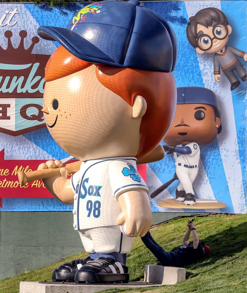 A fan rests in the shadow of the Freddy Funko statue on Funko Friday at Funko Field in Everett on July 12, 2019. (Kevin Clark / The Herald)
