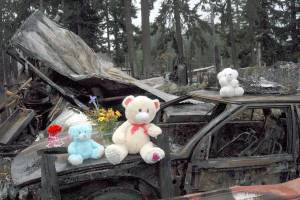 A memorial of teddy bears and flowers sits Wednesday atop a burned car near where the bodies of Valerie Kambeitz, 34, and her children, Lilly Kambeitz, 9, Emma Kambeitz, 6, and Jayden Kambeitz, 5, were discovered after a mobile home fire Saturday at the Welcome Inn RV Park in Port Angeles. (Keith Thorpe/Peninsula Daily News)