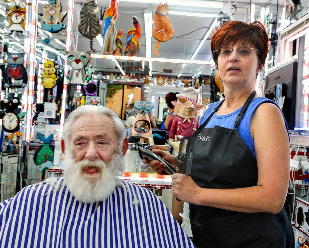 Surrounded by whimsical decor, Barber Stop Shop customer Jim Blubaugh gets a trim from Brenda Humbert. (Dan Bates / The Herald)