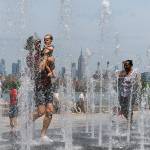 People enjoy the day playing in a water fountain as the Empire State Building is seen from Williamsburg section of Brooklyn on Saturday in New York. Americans from Texas to Maine sweated out a steamy Saturday as a heat wave spurred cancelations of events from festivals to horse races and the nations biggest city ordered steps to save power to stave off potential problems. (AP Photo/Eduardo Munoz Alvarez)