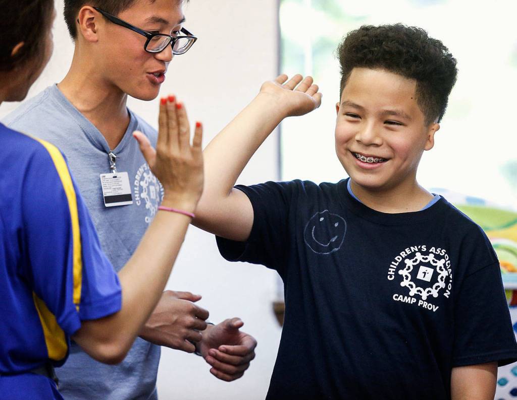 Anthony Vu, a 15-year-old volunteer at Camp Prov, looks on as a camper high-fives a unit leader at Forest Park Wednesday. (Dan Bates / The Herald)
