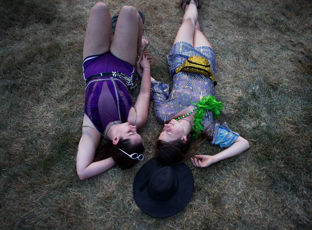 Xoe Heaney, left and Sarah Bilchak, right, hold hands and relax during the opening ceremony at the first day of Summer Meltdown on Thursday, Aug. 1, 2019 in Darrington, Wash. (Olivia Vanni / The Herald)