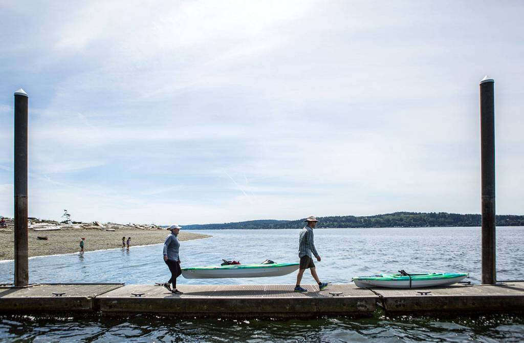 Angela Gonzalez, left, and Juan Gonzalez, right, carry their kayaks out onto the dock at Camano Island State Park. (Olivia Vanni / The Herald)