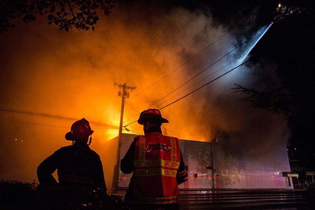 Everett Fire Department firefighters watch as water is sprayed on the Judd & Black appliance store on Sept. 21, 2018, in Everett. (Olivia Vanni / Herald file)