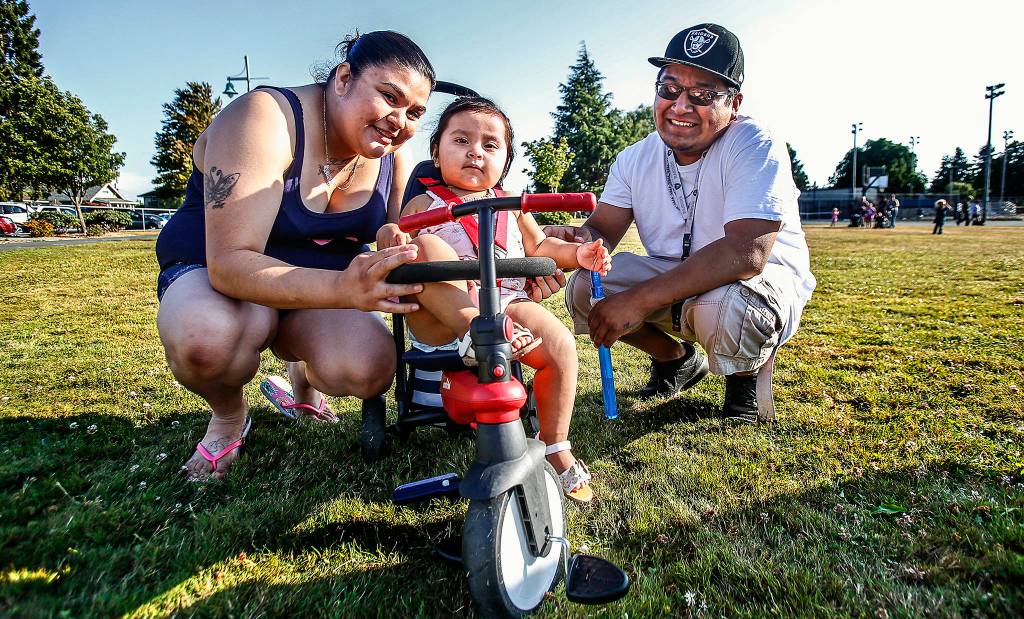 Mariah Martinez and Juan Osorio-H brought their 1-year-old daughter Janali Osorio and her trike out to the Riverside Neighborhood gathering at Garfield Park. (Dan Bates / The Herald)