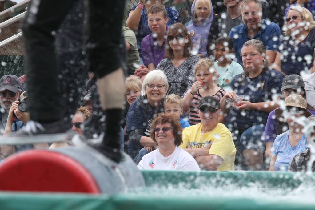 Audience members watch as two lumberjack compete in a log rolling event during the International Lumberjack Show on opening day of the Evergreen State Fair on Thursday, Aug. 22, 2019 in Monroe, Wash. The cabin is the first building to be placed on the Snohomish County Register of Historic Places. (Andy Bronson / The Herald)