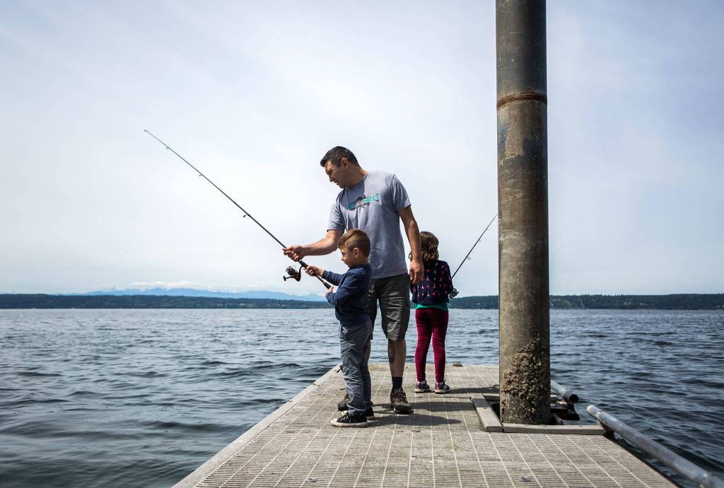 Gino Sanita (center) teaches his son Carlo, 5, and daughter Virgina, 7, how to fish off of the boat launch dock at Camano Island State Park on June 9. (Olivia Vanni / The Herald)