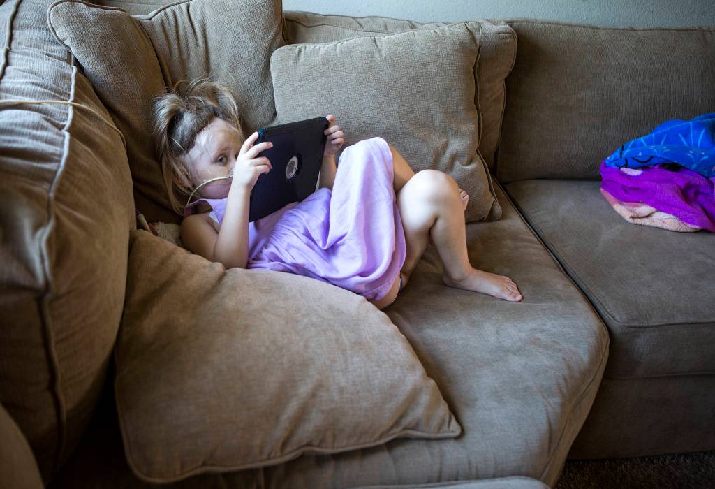 <a href="https://www.heraldnet.com/life/fundraiser-to-help-4-year-old-marysville-girl-fighting-cancer/" target="_blank">Sadie Sheldon</a> hides behind her iPad as she watches YouTube Kids at her home on Aug. 15 in Marysville. (Olivia Vanni / The Herald)