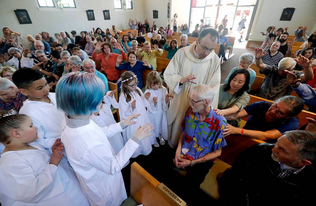 Robert Fuller (seated center right) receives a blessing and prayer from Rev. Quentin Dupont on May 5, among white-robed children who had just received their first communion and the congregation at St. Therese Parish Catholic church in Seattle. (AP Photo/Elaine Thompson)