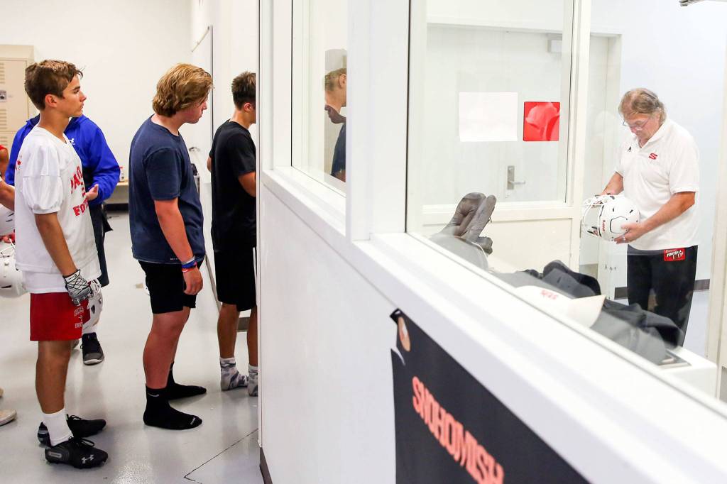 Players wait to have their helmets examined by assistant coach Craig Smith in order to receive their S decals on Aug. 30 at Snohomish High School. (Kevin Clark / The Herald)