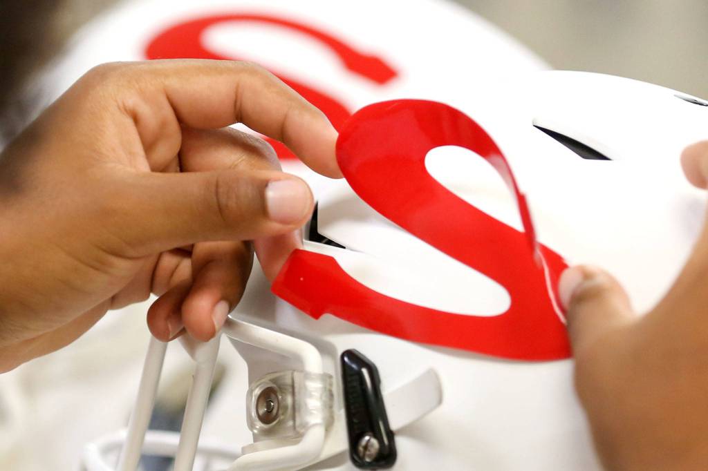Snohomish S decals are applied to newly cleaned helmets on Aug. 30. (Kevin Clark / The Herald)