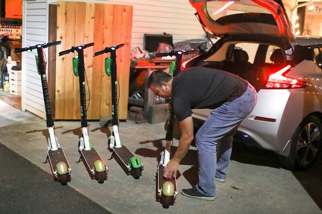 Dan Baer unloads e-scooters as his wife wheels them into a their garage for charging. (Lizz Giordano / The Herald)
