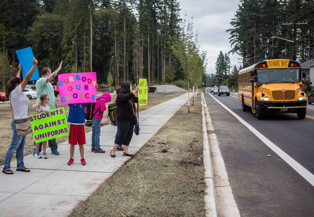 Protestors wave at a school bus driving by on Wednesday, outside of Tambark Creek Elementary School near Bothell. (Olivia Vanni / The Herald)