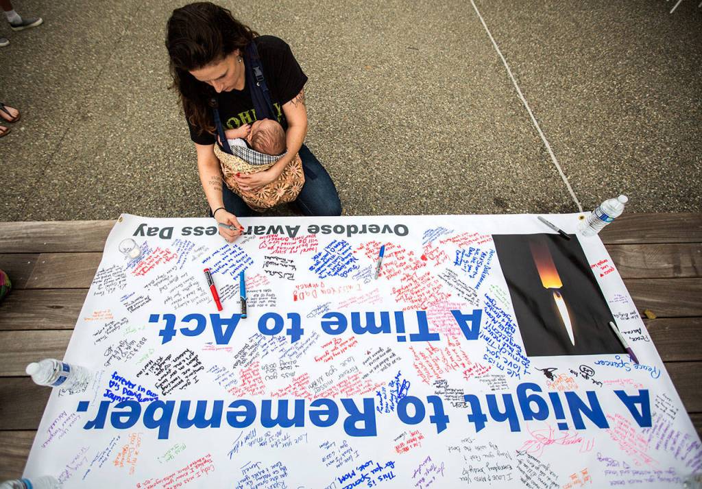 Johanna Sellers holds her son Amado, 6 weeks, who is named after a friend who died of a drug overdose, whole signing a banner during Snohomish Overdose Preventions A Night to Remember on Thursday in Everett. (Olivia Vanni / The Herald)