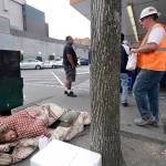 In this May 2018 photo, a man sleeps on the sidewalk as people behind line up to buy lunch at a Dicks Drive-In restaurant in Seattle. (AP Photo/Elaine Thompson, File)