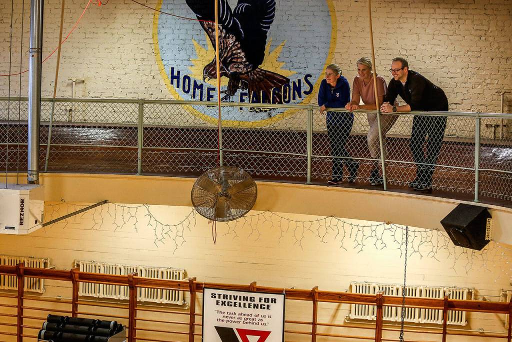 A Home of the Falcons painting still graces the bricks high on a wall at one end of the Everett Ys 1920s gym. Long ago, the Falcons were YMCA basketball teams. From left Gael Gebow, Kristy Kentch and Zac Jagow, all Y staff members, look down on the vintage gymnasium from a wooden running track. (Dan Bates / The Herald)
