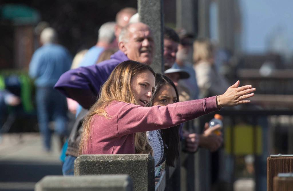 A woman explains to a friend how the bridge goes into place as they watch the installation from the marina pier while the Grand Avenue Park Bridge is slowly rotated into place along Marine View Drive on Wednesday in Everett. (Andy Bronson / The Herald)