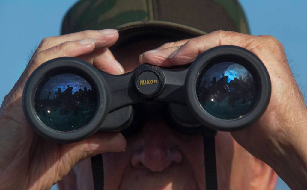 The Grand Avenue Park Bridge is reflected in Mack Hyatts binoculars as he waits for it to be rotated into place on Wednesday in Everett. (Andy Bronson / The Herald)