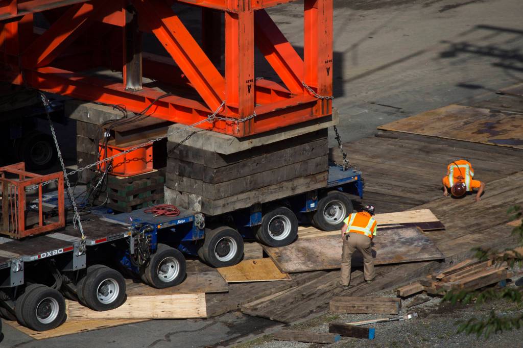 Workers peer under the wheels as the $20 million Grand Avenue Park Bridge rolls over dunnage to keep the wheels from sinking into the earth as it was slowly rotated into place along Marine View Drive on Wednesday in Everett. (Andy Bronson / The Herald)