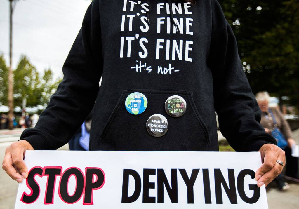 A protestor wears a sweatshirt and pins protesting climate change denial during the die-in for climate action at the Snohomish County Campus Plaza on Friday in Everett. (Olivia Vanni / The Herald)