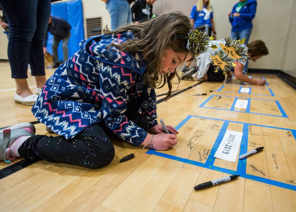 Ada Pembroke, 7, signs part of the floor in the 60s Gym during the YMCAs time capsule ceremony on Saturday, Sept. 21, 2019 in Everett, Wash. (Olivia Vanni / The Herald)