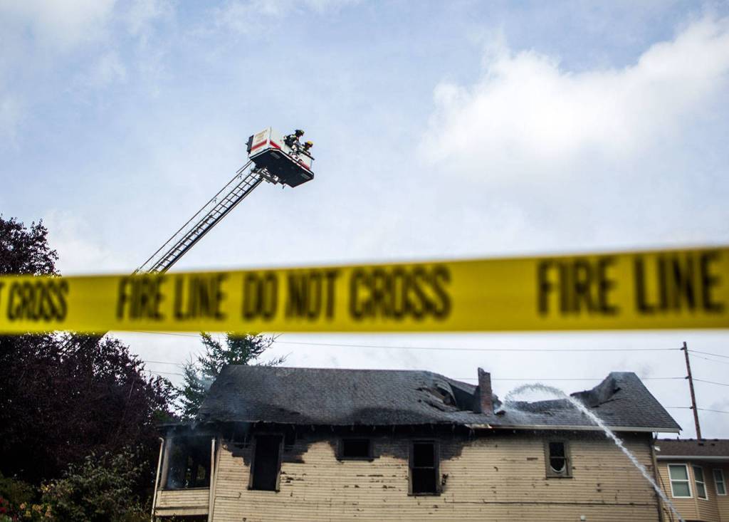 Firefighters on a ladder truck look down on the collapsed roof of a home that erupted in flames Thursday morning in Everett. (Olivia Vanni / The Herald)