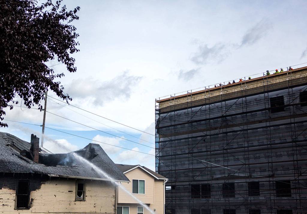 Construction workers watch from the top of a building while water is sprayed on a house that caught fire. (Olivia Vanni / The Herald)