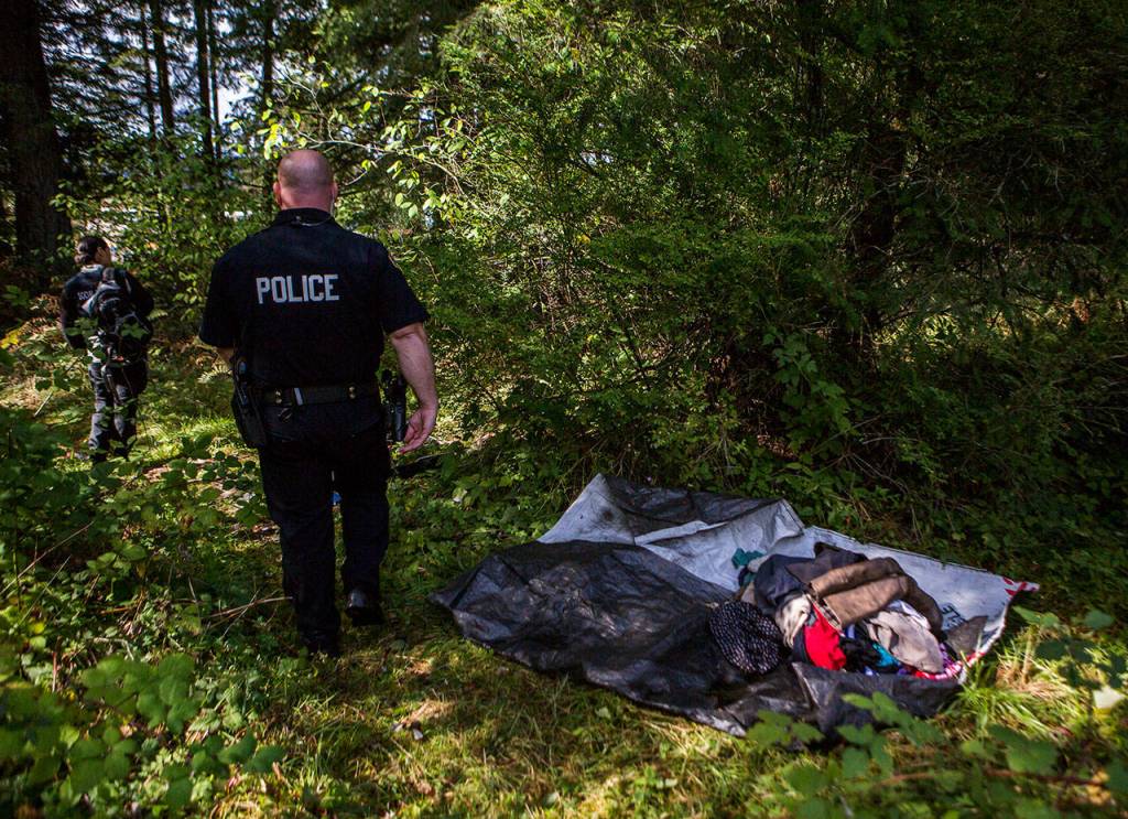 Social worker Elisa Delgado (left) and Officer Justin Springer (right) walk through a recently cleared out homeless encampment on Thursday in Monroe. (Olivia Vanni / The Herald)