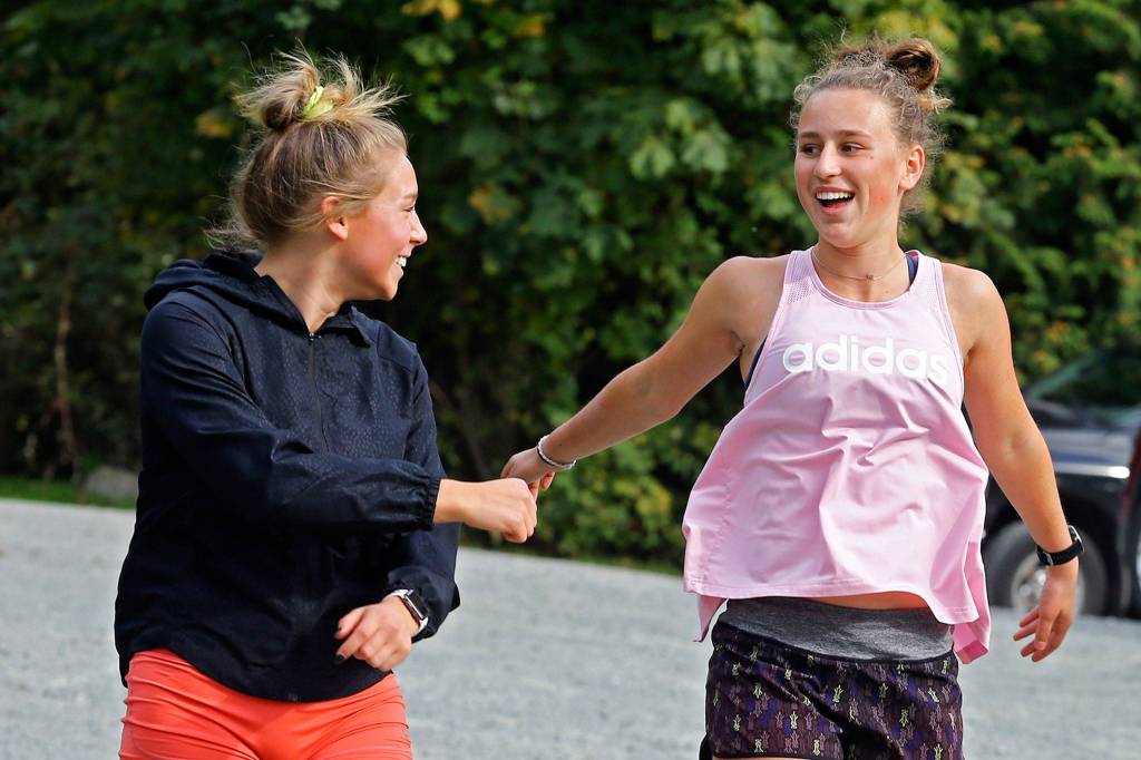Glacier Peaks Alexis Palmer (left) and Lindsay Ardry shares a laugh during warmups before running on Oct. 2, 2019, at Lord Hill Regional Park in Snohomish. (Kevin Clark / The Herald)