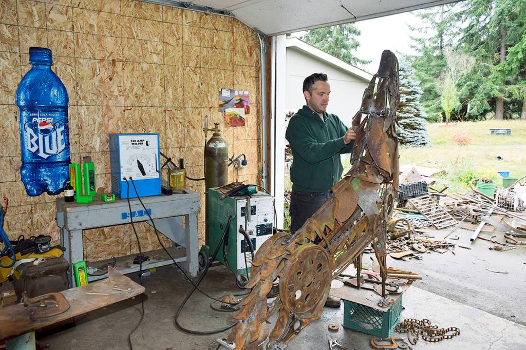 In his Clinton garage studio, Aidan Rayner works on his howling wolf sculpture comprising discarded machine parts, tools and other metal found at Island Recycling. The artwork is slated to be a memorial for his twin brother, Dylan Rayner, who died in 2016. (Patricia Guthrie / South Whidbey Record)