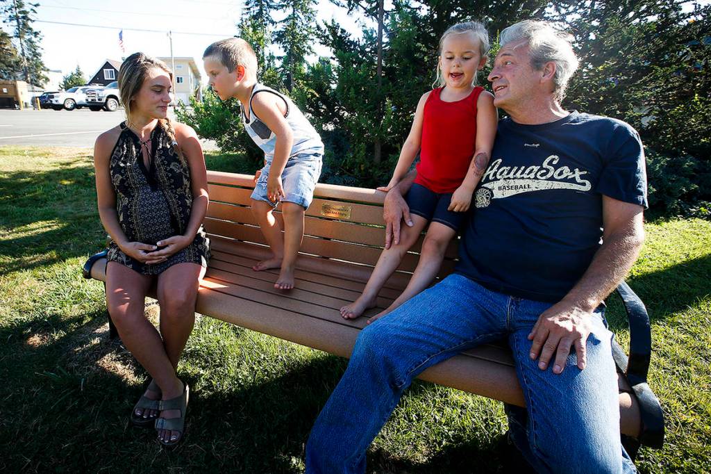 This 2016 photo shows Matt Hartman (right) with his grandkids, Brooklyn (next to him) and Brock, and Chelsea Lewis (on the far left), on a memorial bench he built for his late wife, Dori Murry, on the southwest corner of a park in Granite Falls. (Ian Terry / Herald file)
