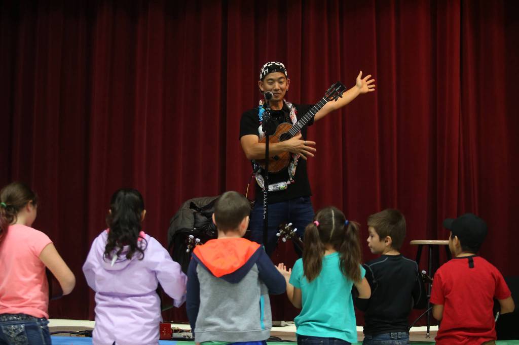Jake Shimabukuro shows students how to strum an open chord with one hand. (Andy Bronson / The Herald)