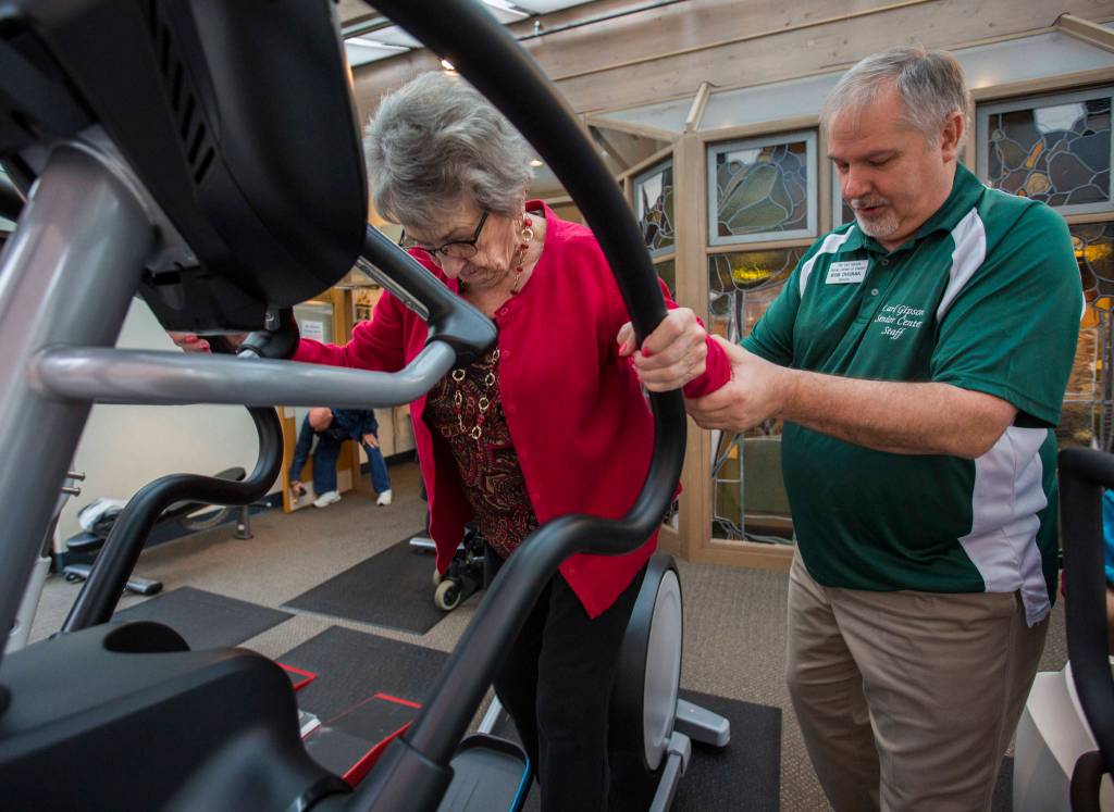 Bob Dvorak helps Doris Moran onto the elliptical at the Carl Gipson Senior Centers new fitness room. (Olivia Vanni / The Herald)
