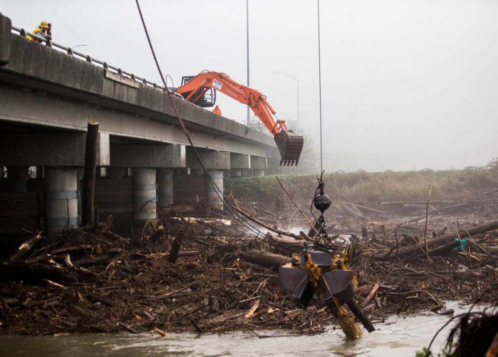 An excavator attempts to push logs out of the way along the eastbound lanes of State Route 2 on Wednesday in Everett. (Olivia Vanni / The Herald)