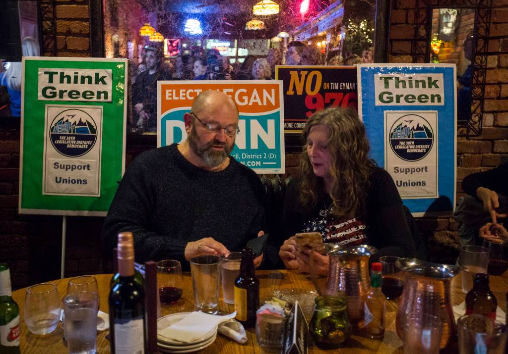 Bill Sheets and Ardis Hallanger are surrounded by signs as they check their phones as the first numbers come in on election night at the Vintage Cafe in Everett. (Olivia Vanni / The Herald)