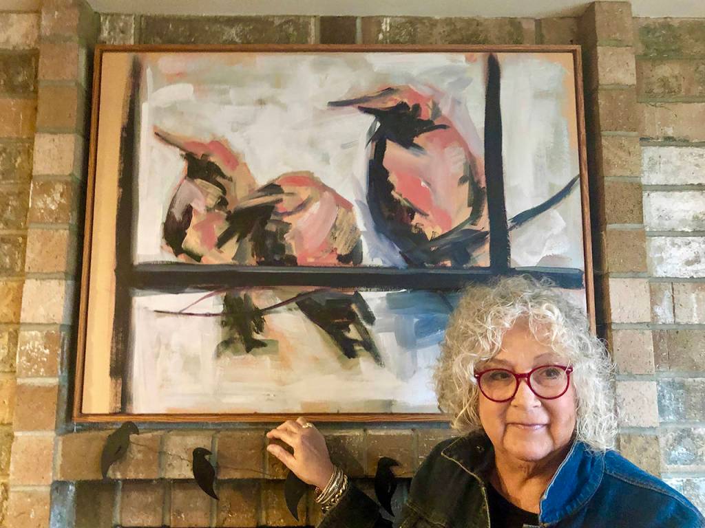 Sharen Heath stands in front of the crow painting that sparked her obsession to collect birds in various forms and put some giant ones in the front yard of her Langley home. (Andrea Brown / The Herald)