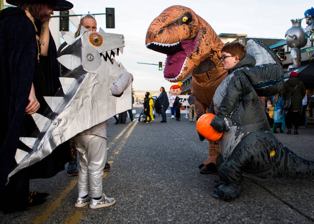 A group of people in dinosaur costumes greet each other during Downtown Trick-or-Treating on Oct. 31, 2019 in Everett, Wash. (Olivia Vanni / The Herald)