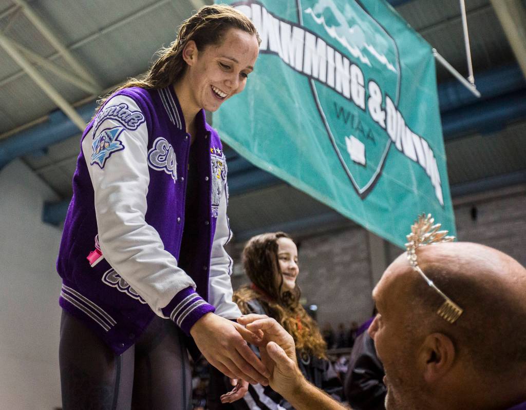 Kamiak senior Elli Straume smiles and shakes hands with coach Chris Erickson as she stands on the podium following her 200 freestyle triumph. (Olivia Vanni / The Herald)