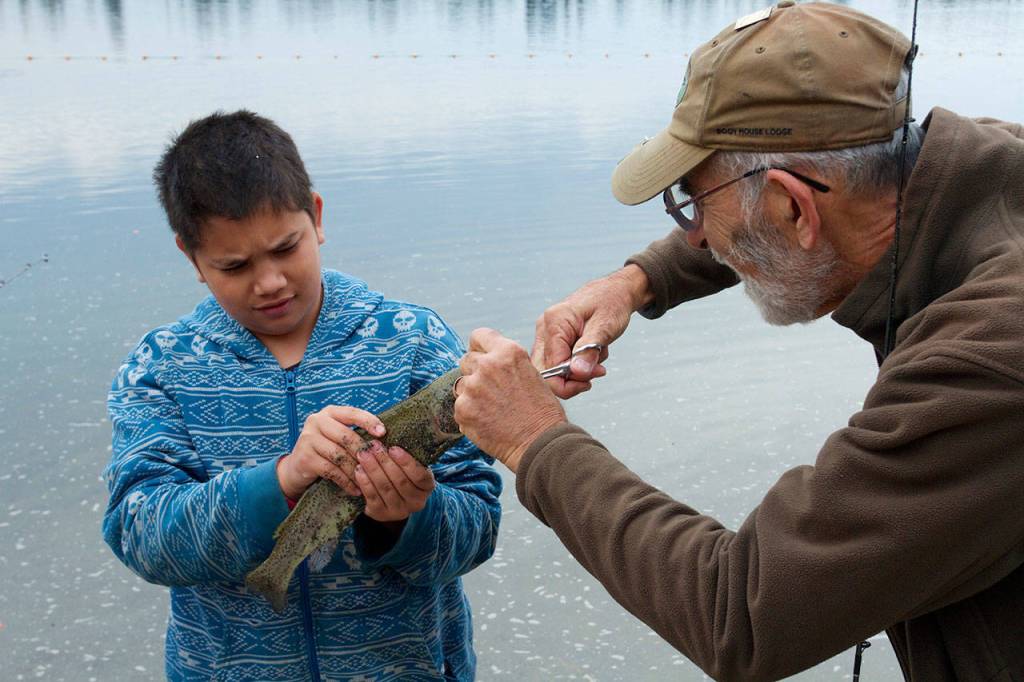Ron Pera of Camano Island helps a youngster land his fish during a fish-in at Silver Lake in Everett. (Photo by Mike Benbow)