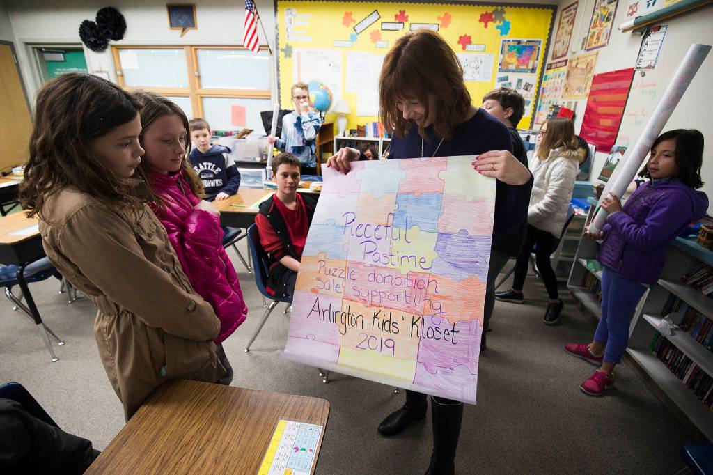 Fifth-grade students at Kent Prairie Elementary School in Arlington show Suzie Nelson posters they made for a fundraiser featuring more than 100 Christmas-themed jigsaw puzzles made by Nelson and Sonya Shipley. (Andy Bronson / The Herald)