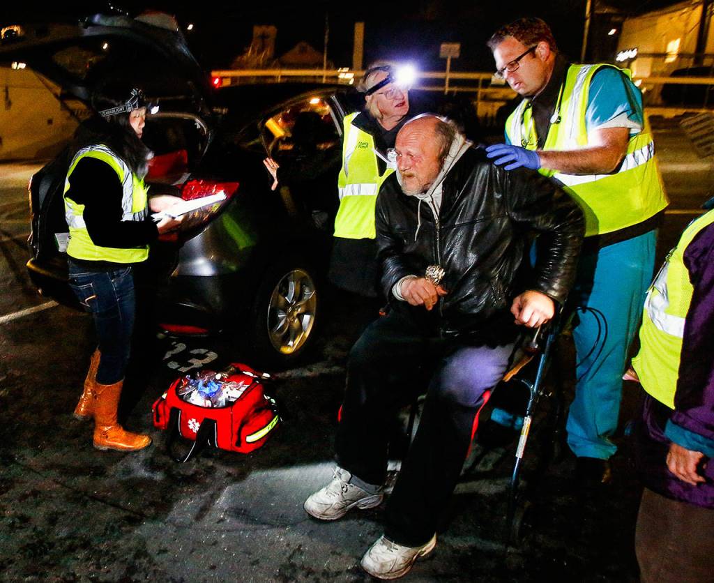 A man in a walker gets medical attention from MercyWatch volunteers Dr. Jimmy Grierson (right) and nurse Gail Pyper while medical scribe Amanda Dahl takes down information. (Dan Bates / The Herald)