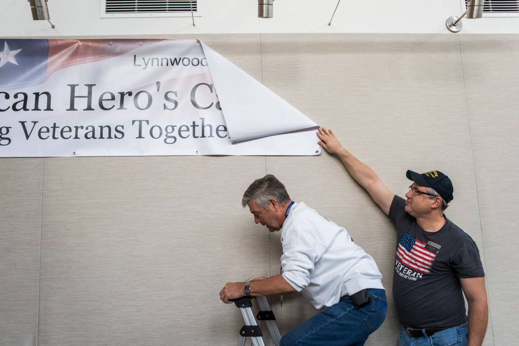 Volunteer Chris Szarek (right) holds up the Heros Cafe banner as Steve Pennington climbs the ladder to finish hanging it before the start of the Heros Cafe at the Verdant Community Wellness Center on Nov. 26. (Olivia Vanni / The Herald)