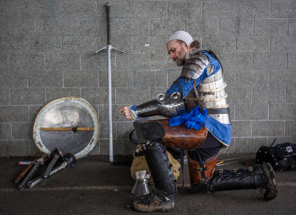 Live action role player Douglas West kneels while donning his armor for combat practice. (Olivia Vanni / The Herald)