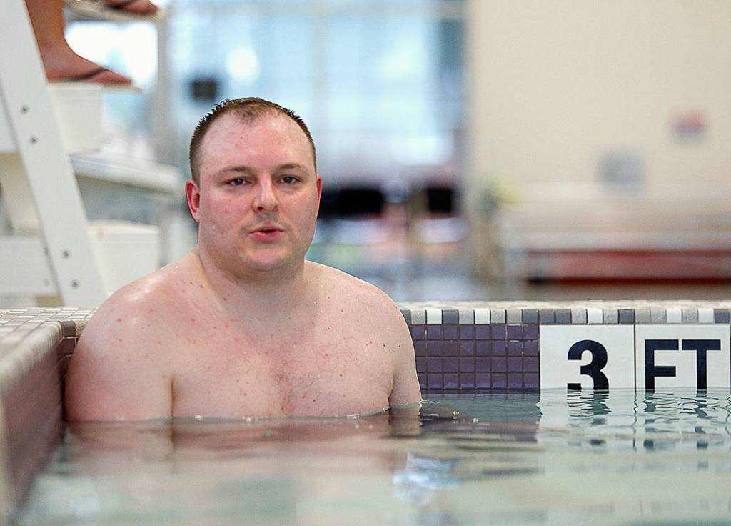 Sheldon Frye relaxes in a hot tub at the new Everett Family YMCA aquatic facility while his wife and two of their three children play in the recreation pool. (Dan Bates / The Herald)